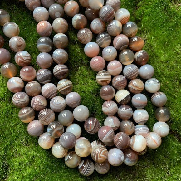 10mm smooth round Botswana agate bead strands on green background 