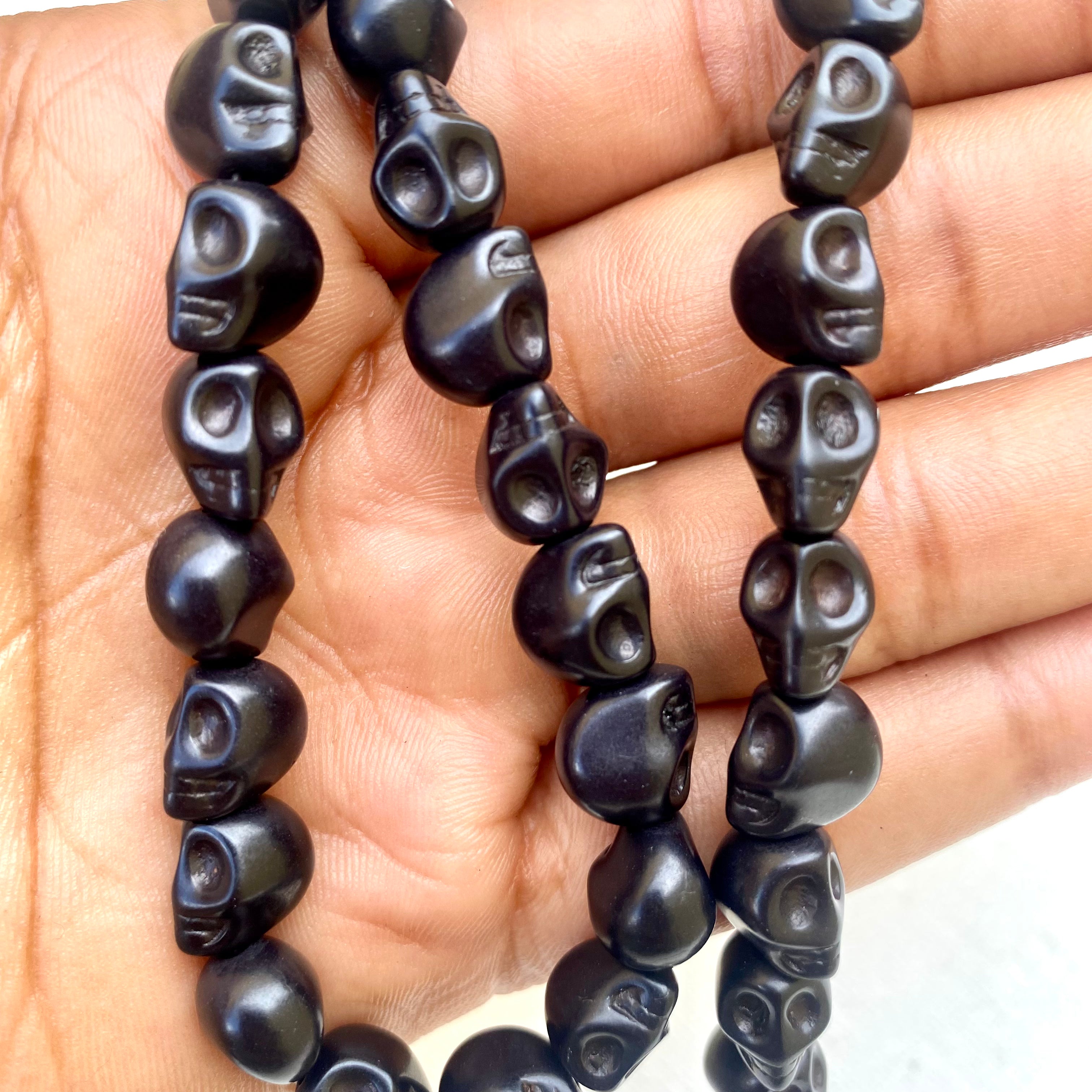 black skull carved stone bead strand draped over hand on white background. 