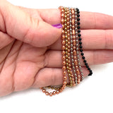 stainless steel ball chain, copper ball chain, and black ball chain in a hand on a white background