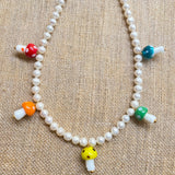 red, orange, yellow, green, and blue glass mushroom beads on a white pearl necklace with a gold clasp on a tan burlap background