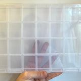 twenty-eight compartment clear plastic bead storage container displayed in a hand over white background. 